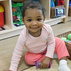 baby girl sitting on floor in classroom smiling holding toy
